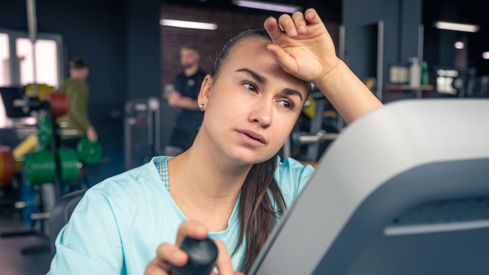 A imagem mostra uma jovem mulher visivelmente cansada e exausta enquanto se exercita em uma academia.